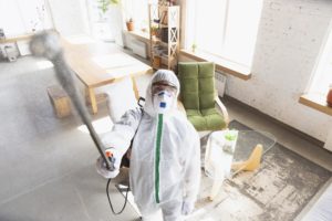 A mold remediation specialist in a full body suite uses a tool to remove mold in a living room.