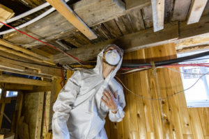A mold remediation specialist in a full body suit examines mold in a crawl space.