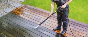 Man cleaning deck with a pressure washer - high water pressure cleaner on wooden deck surface.