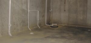 A poured concrete basement with a sump pump in the corner