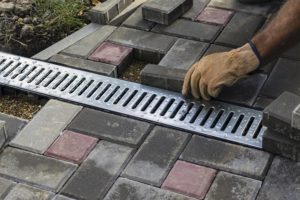 Person laying bricks surrounding an outside drainage system